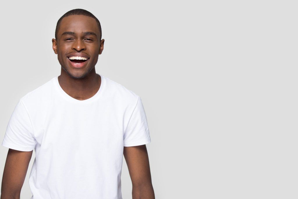 A man in a white t-shirt is laughing with his mouth open.