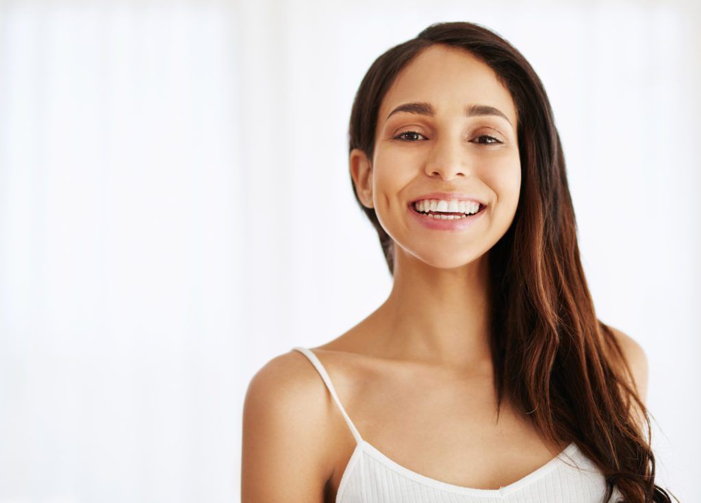 A woman in a white tank top is smiling and looking at the camera.