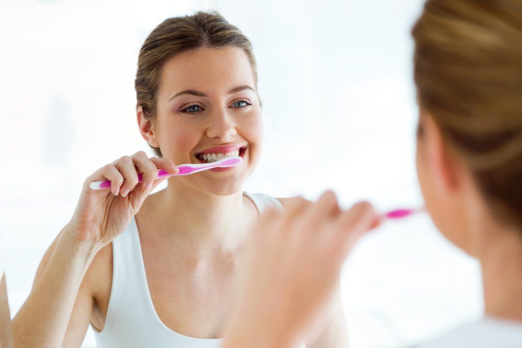 A woman is brushing her teeth in front of a mirror.