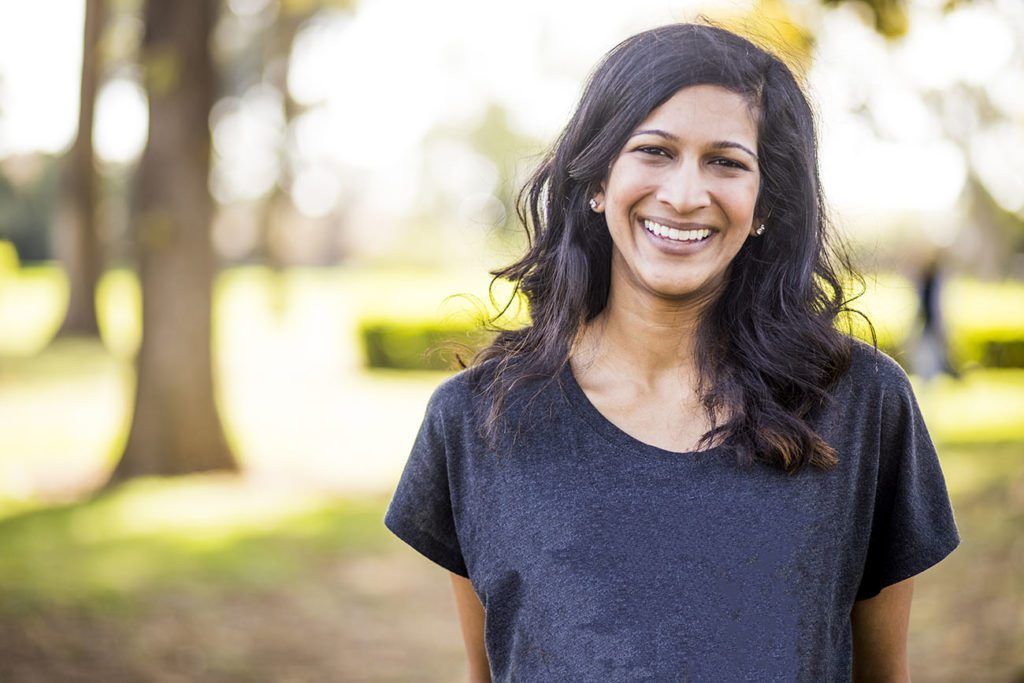 A woman in a black shirt is smiling in a park.
