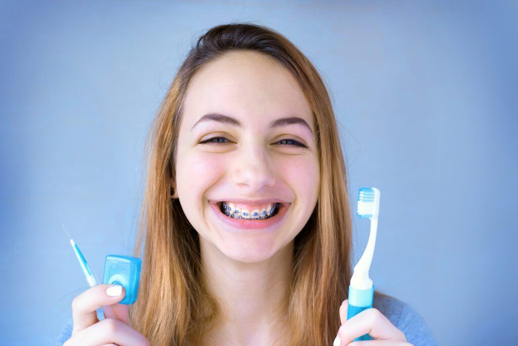 A young woman with braces is holding a toothbrush and floss.