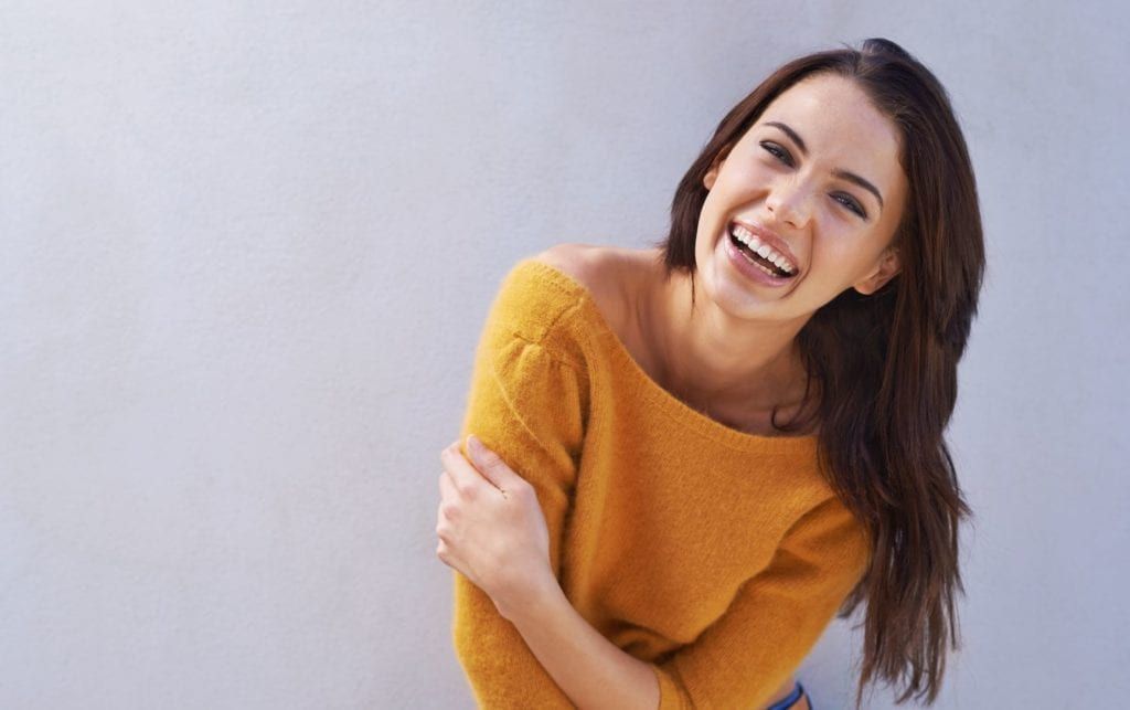 A woman in a yellow sweater is laughing and hugging herself.