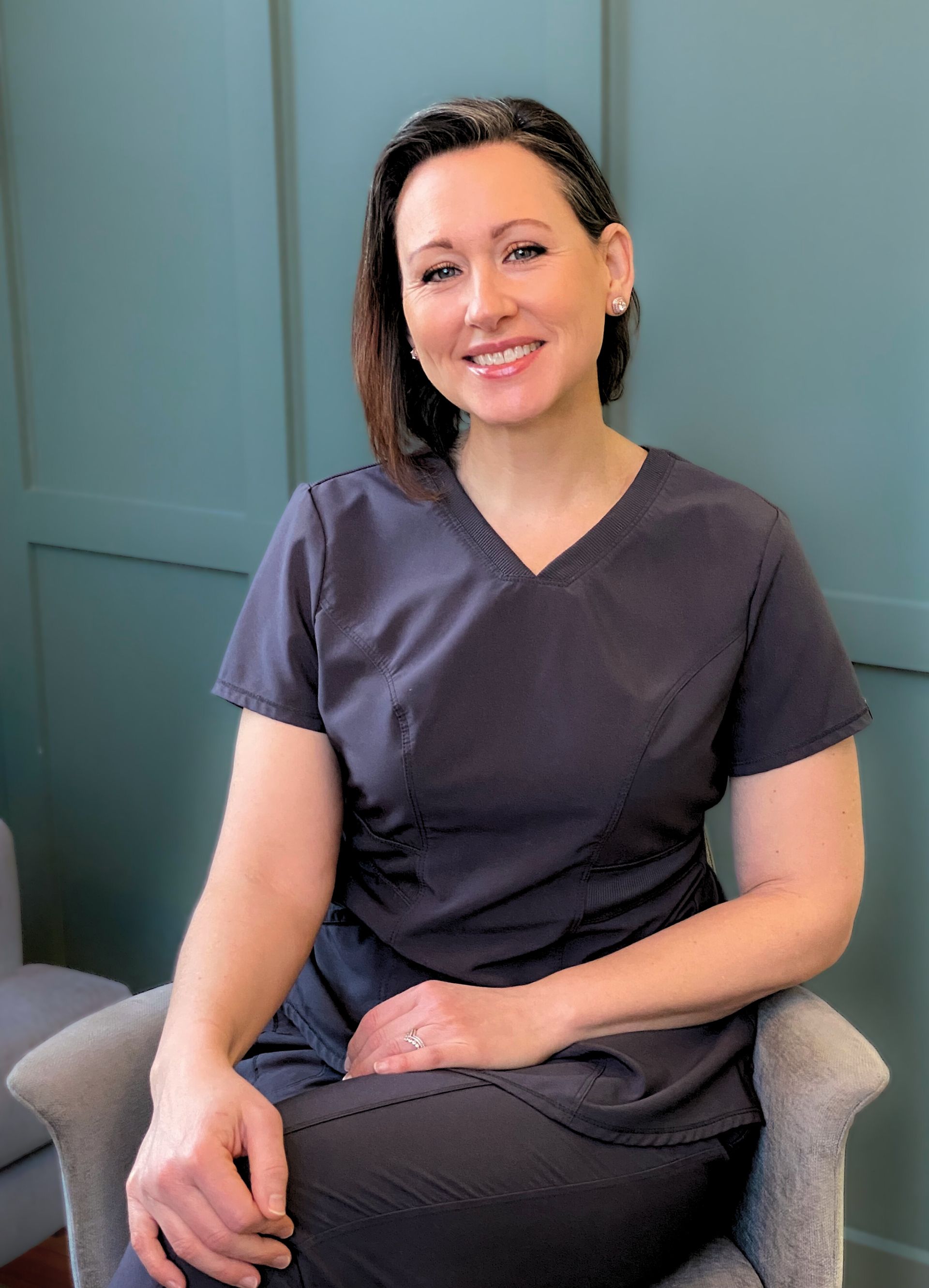 A woman in a scrub is sitting in a chair and smiling.