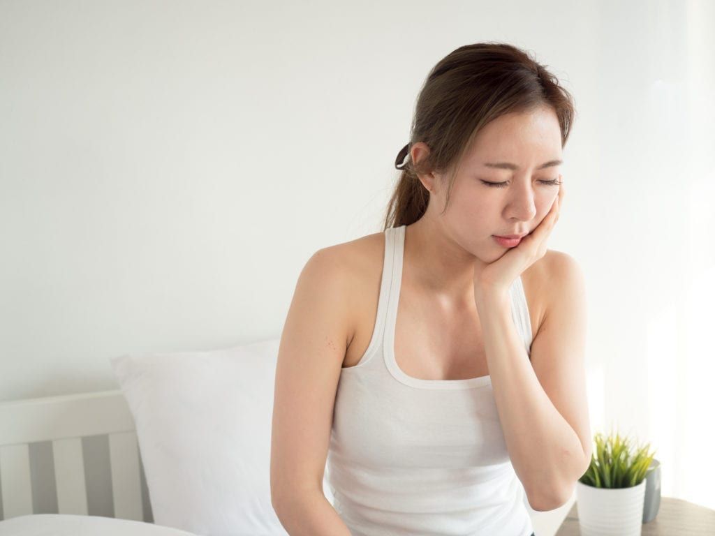 A woman is sitting on a bed with her hand on her face.