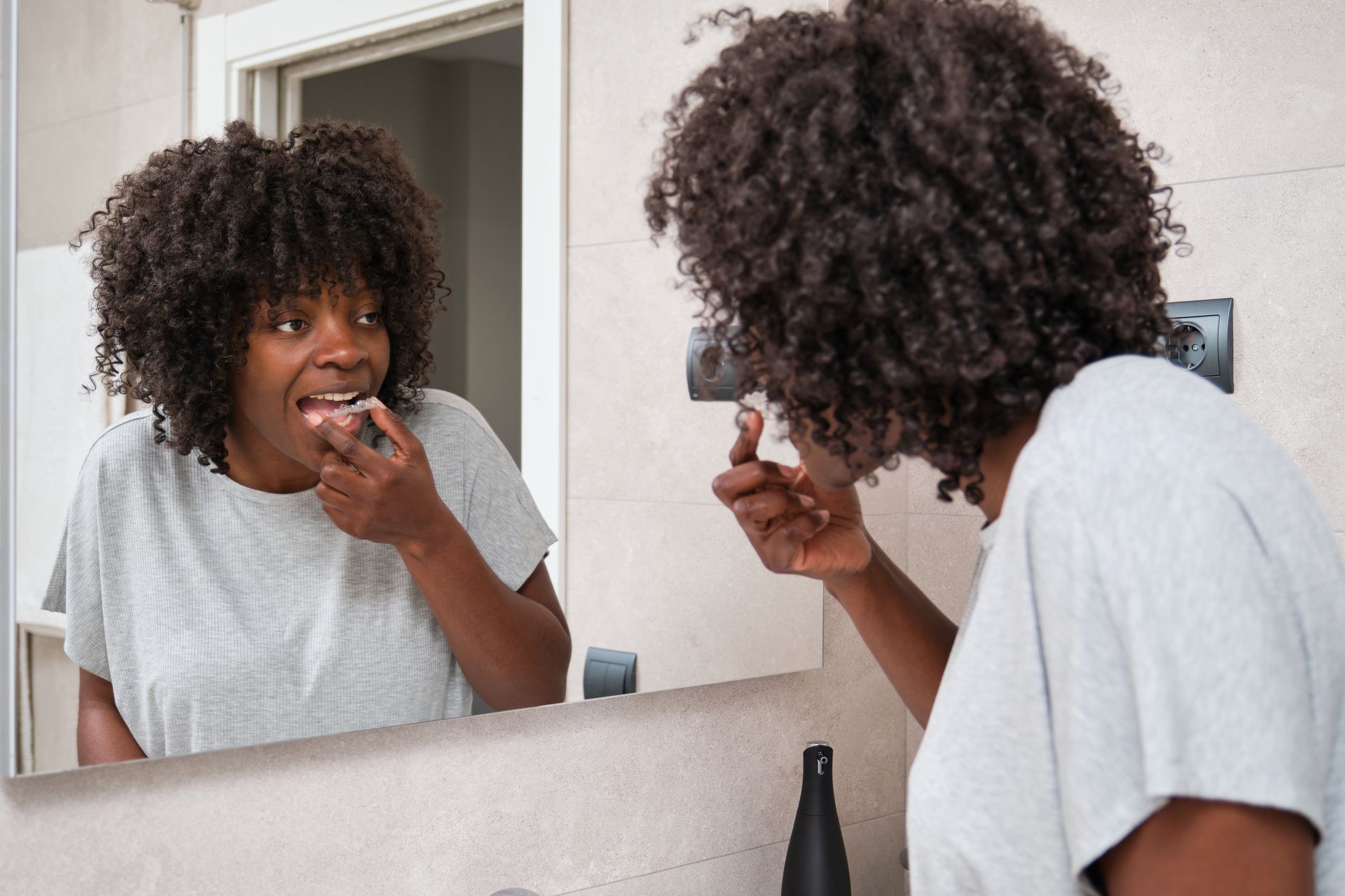 A woman is brushing her teeth in front of a bathroom mirror.