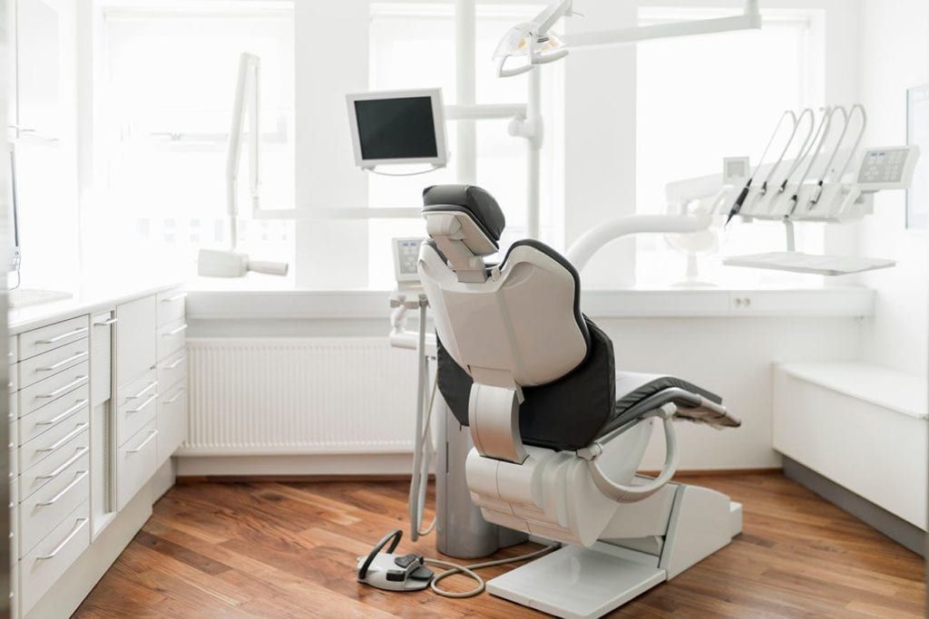 An empty dental office with a dental chair and a monitor.