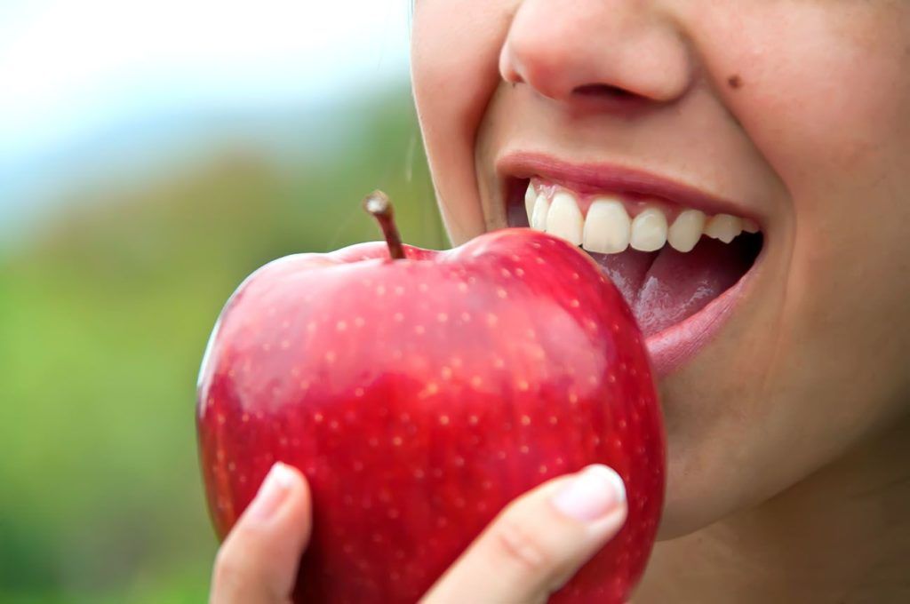A woman is eating a red apple with her mouth open.
