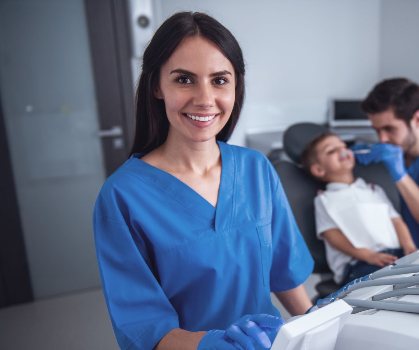 A female dentist is smiling in front of a child in a dental chair.