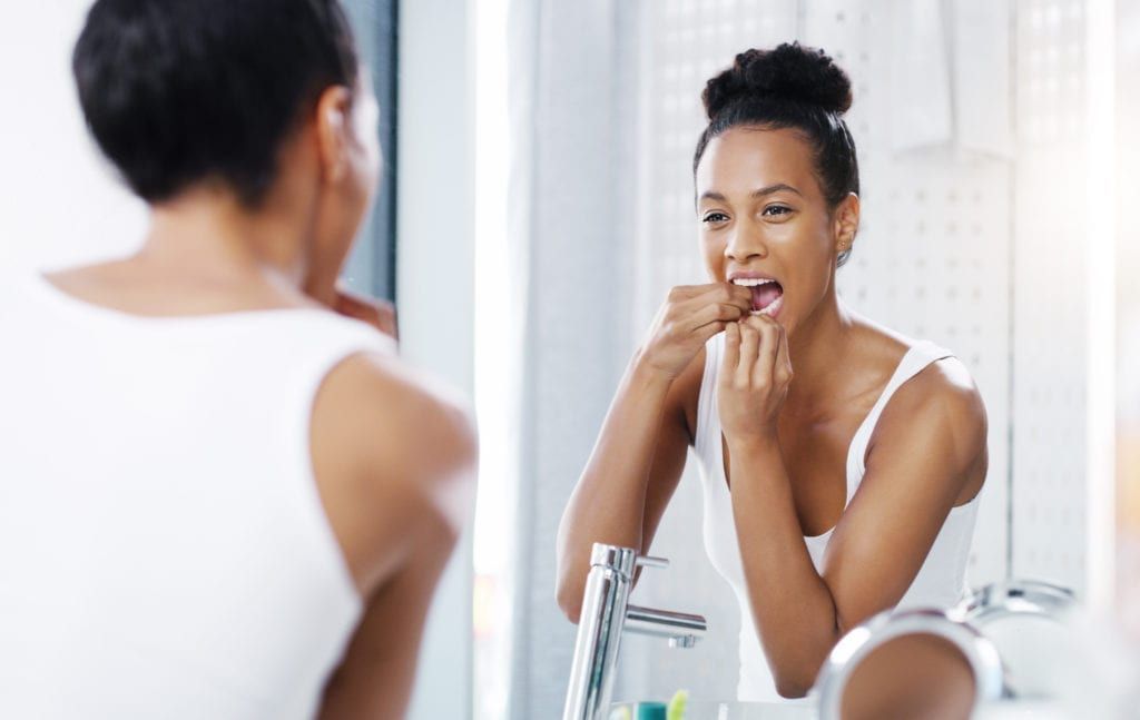 A woman is brushing her teeth in front of a bathroom mirror.