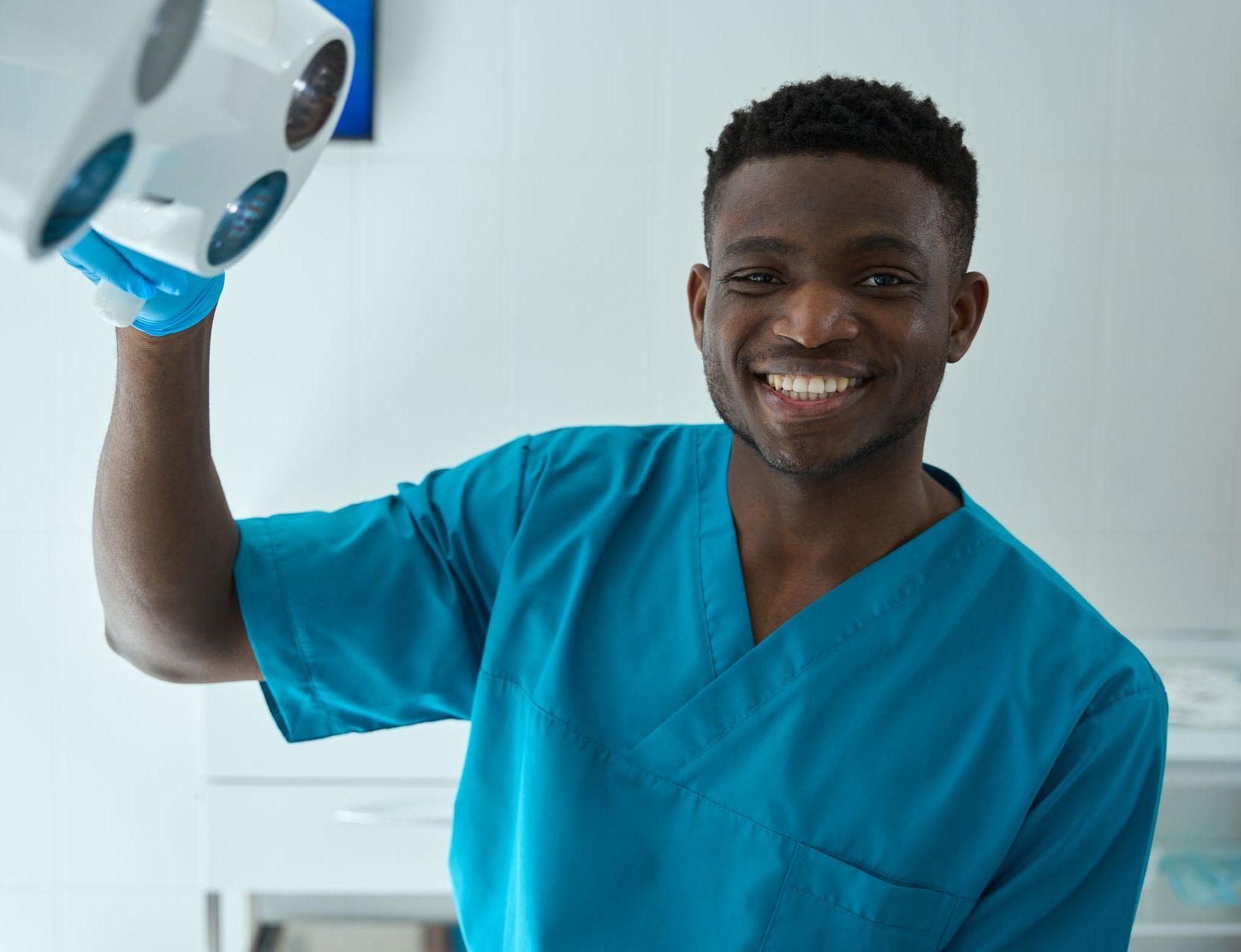 A dentist is smiling while holding a dental mirror in his hand.