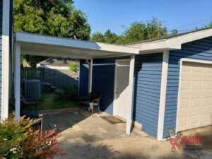A blue house with a white garage door and a canopy over it.