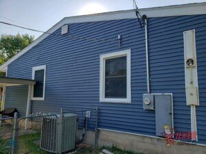 The back of a blue house with white trim and a window.