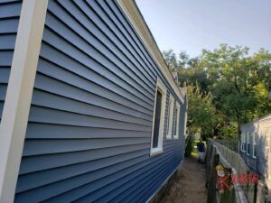 A blue house with a white trim is sitting next to a fence.