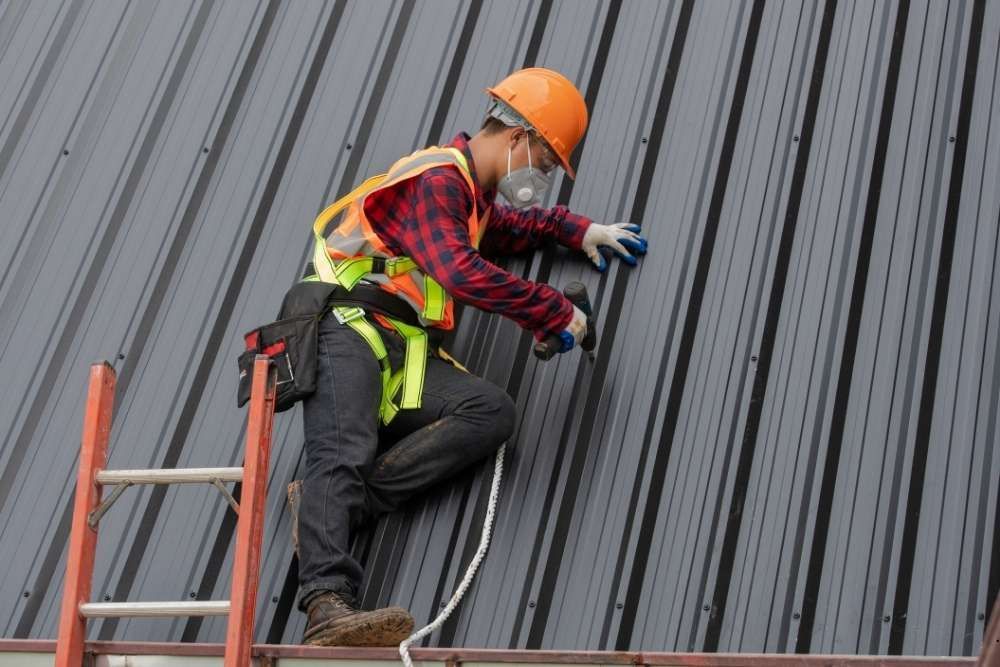 A construction worker is standing on a ladder on top of a roof.