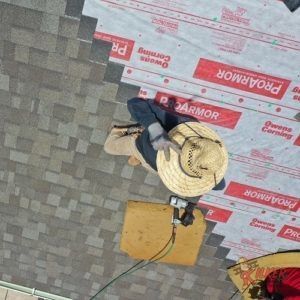 A man wearing a straw hat is working on a proarmor roof