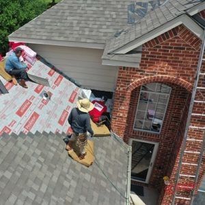 A group of men are working on the roof of a brick house.