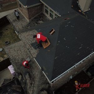 A man in a red shirt is sitting on the roof of a house.