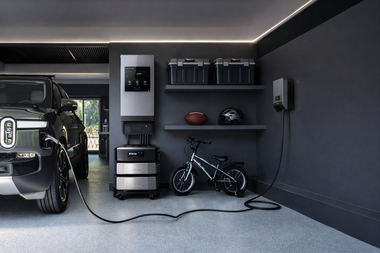 A Rivian truck charging in a modern garage with a modular battery storage system, wall-mounted charger, and bike.