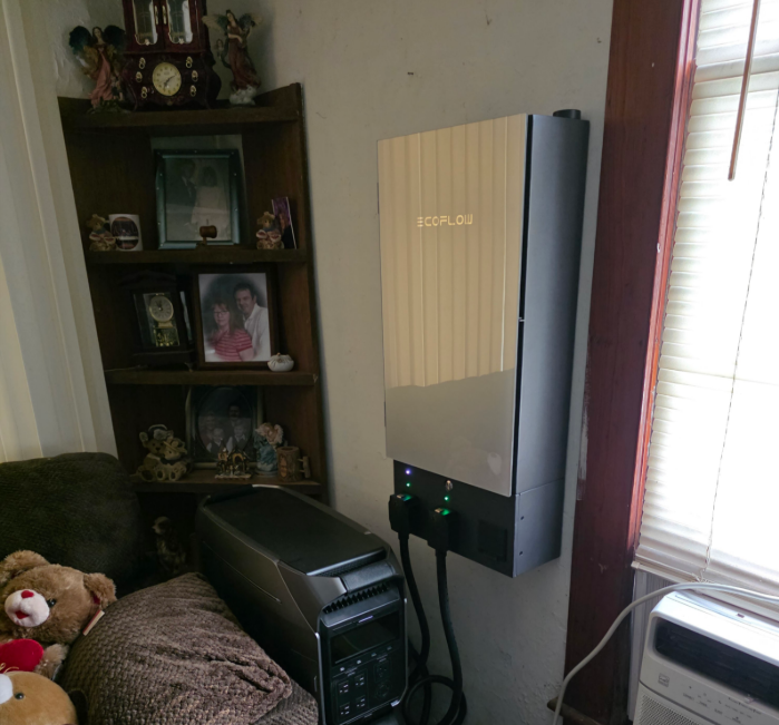 Living room corner with a wall-mounted solar inverter, bookshelf, and window blinds