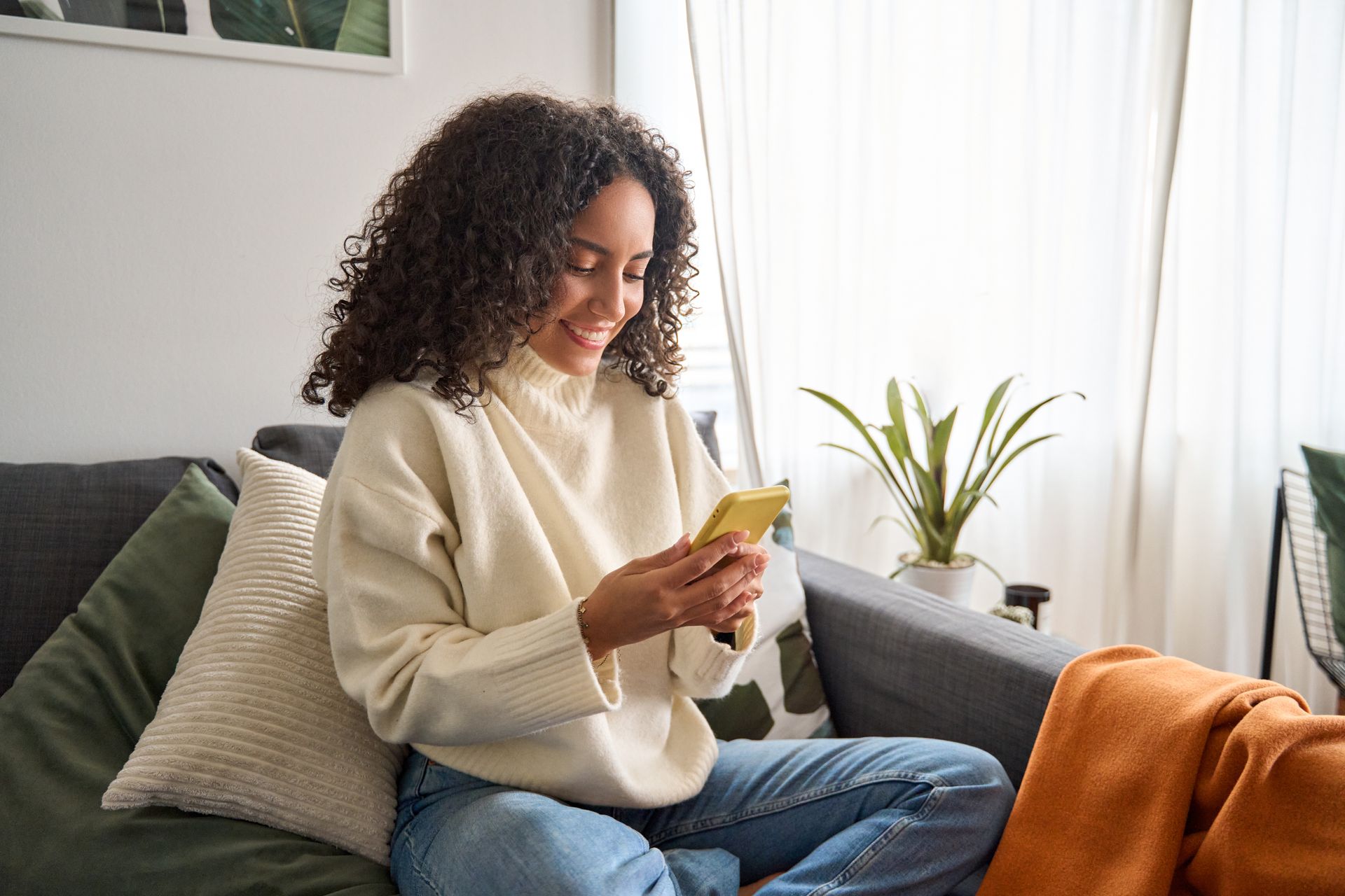 A person using their smartphone to control their motorized window treatments from their couch 