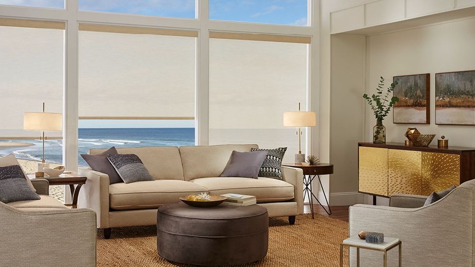 Alta Roller Shades on large, floor-to-ceiling windows in a living room, overlooking a body of water
