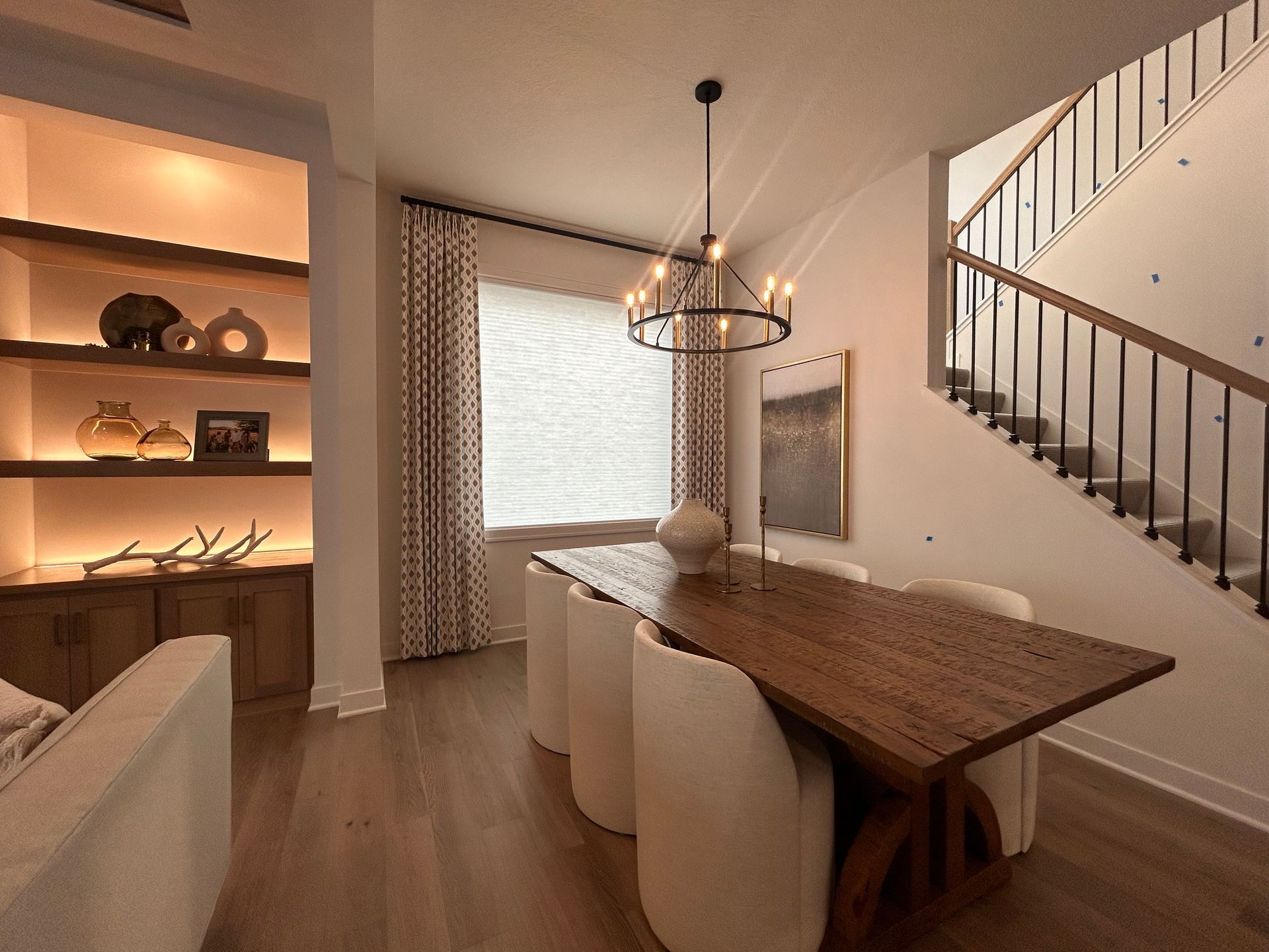 A dining room with a wooden table, chairs and a staircase featuring cellular shades