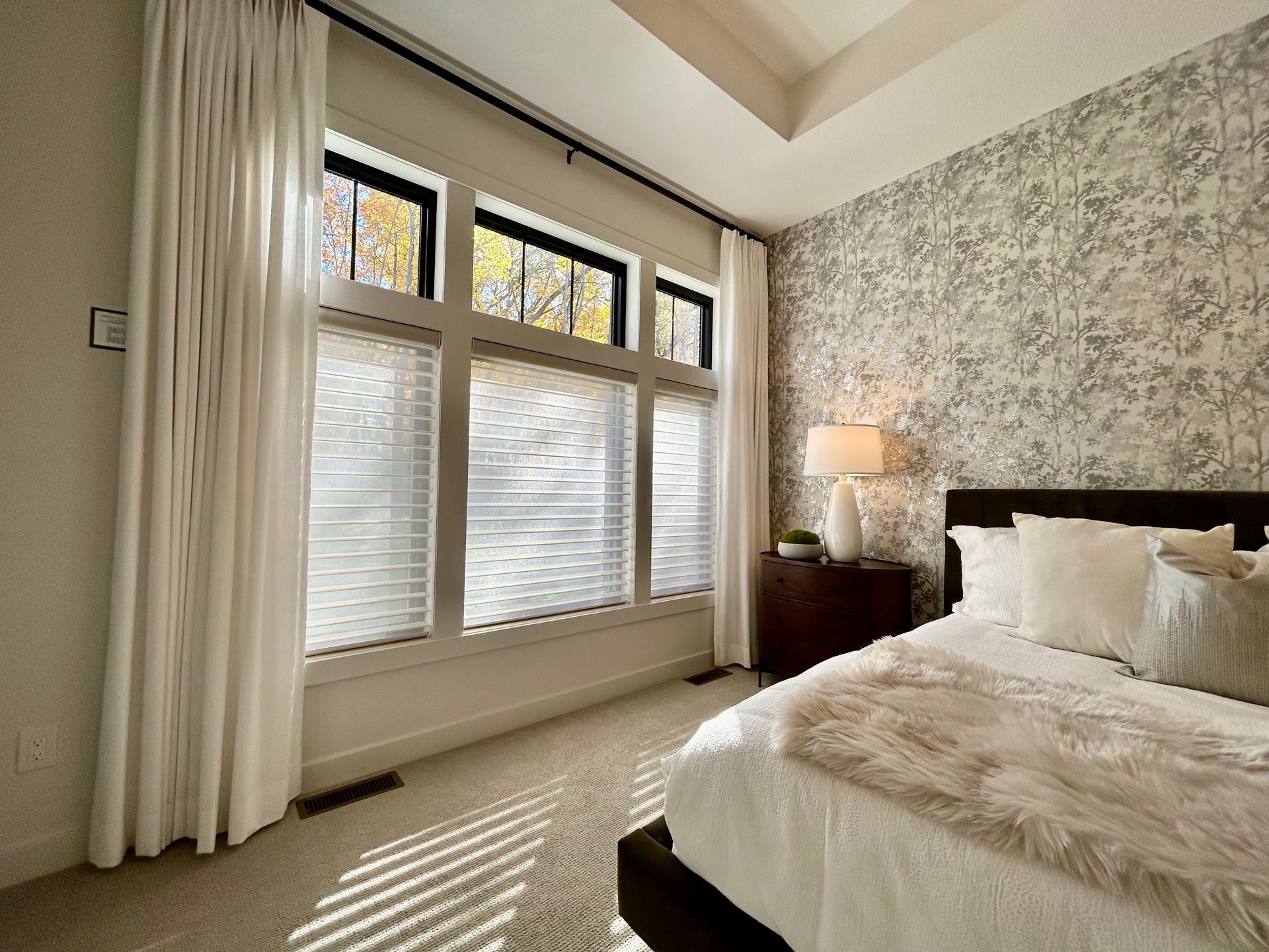 A bedroom with a large bed and lots of windows with sheer shadings