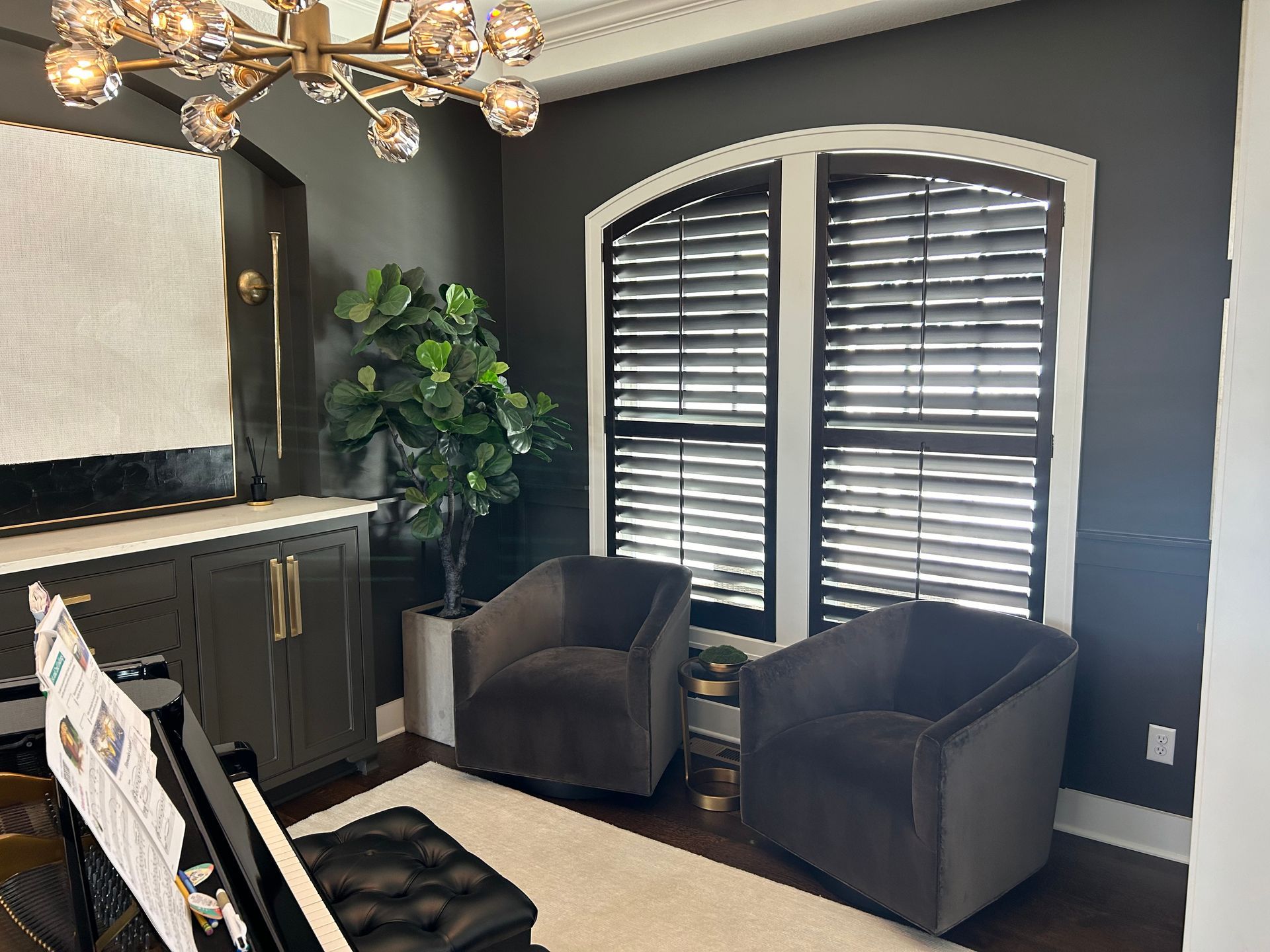 A living room with arched shutters, two chairs, and a piano.