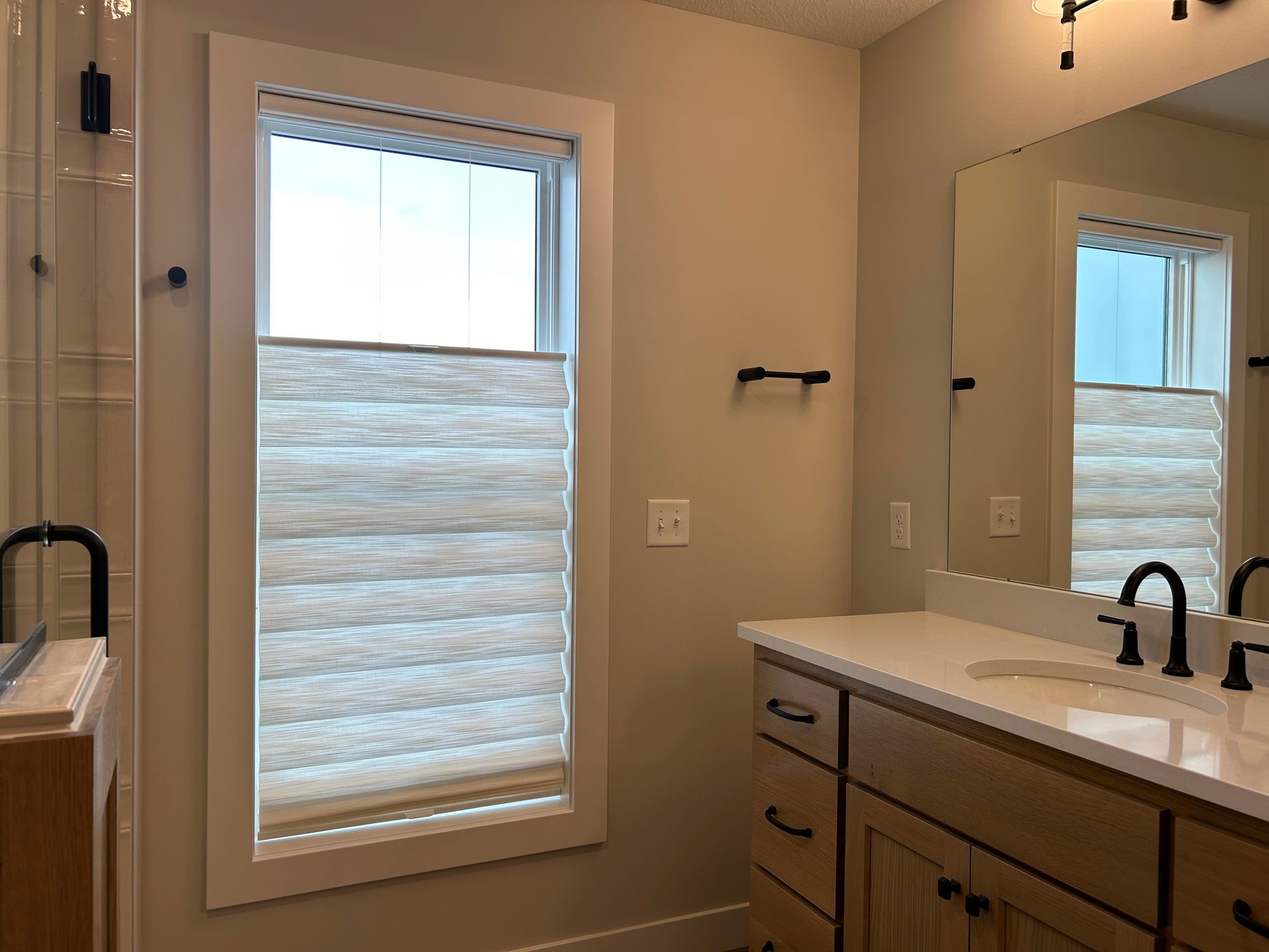 A bathroom with Roman shades, a sink , mirror and two windows.