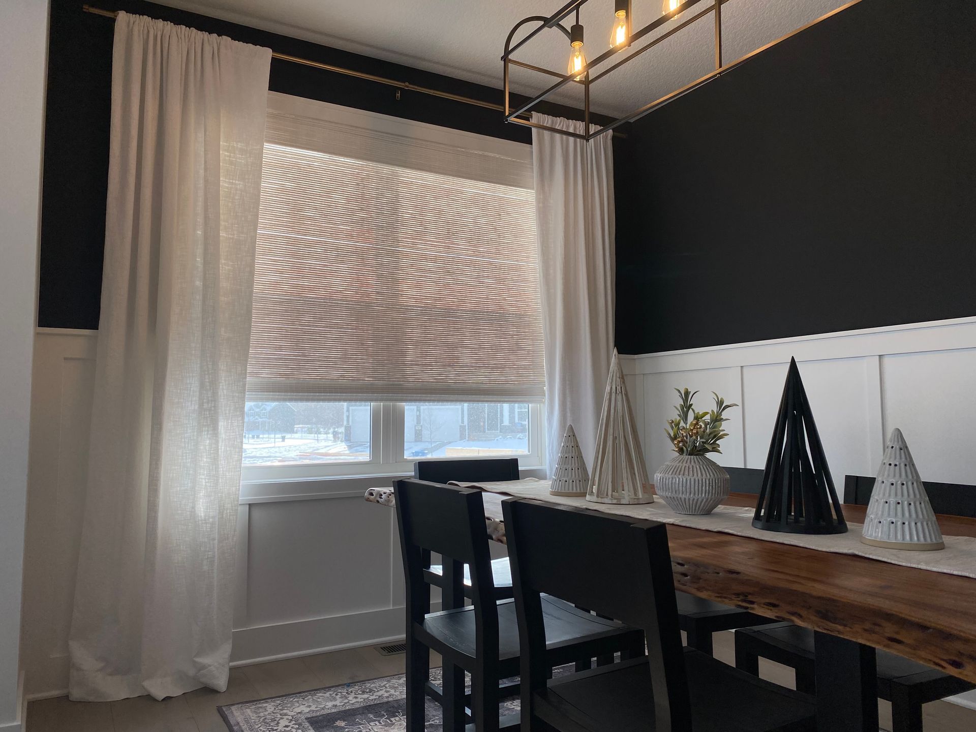 A dining room with a wooden table and chairs and white curtains.