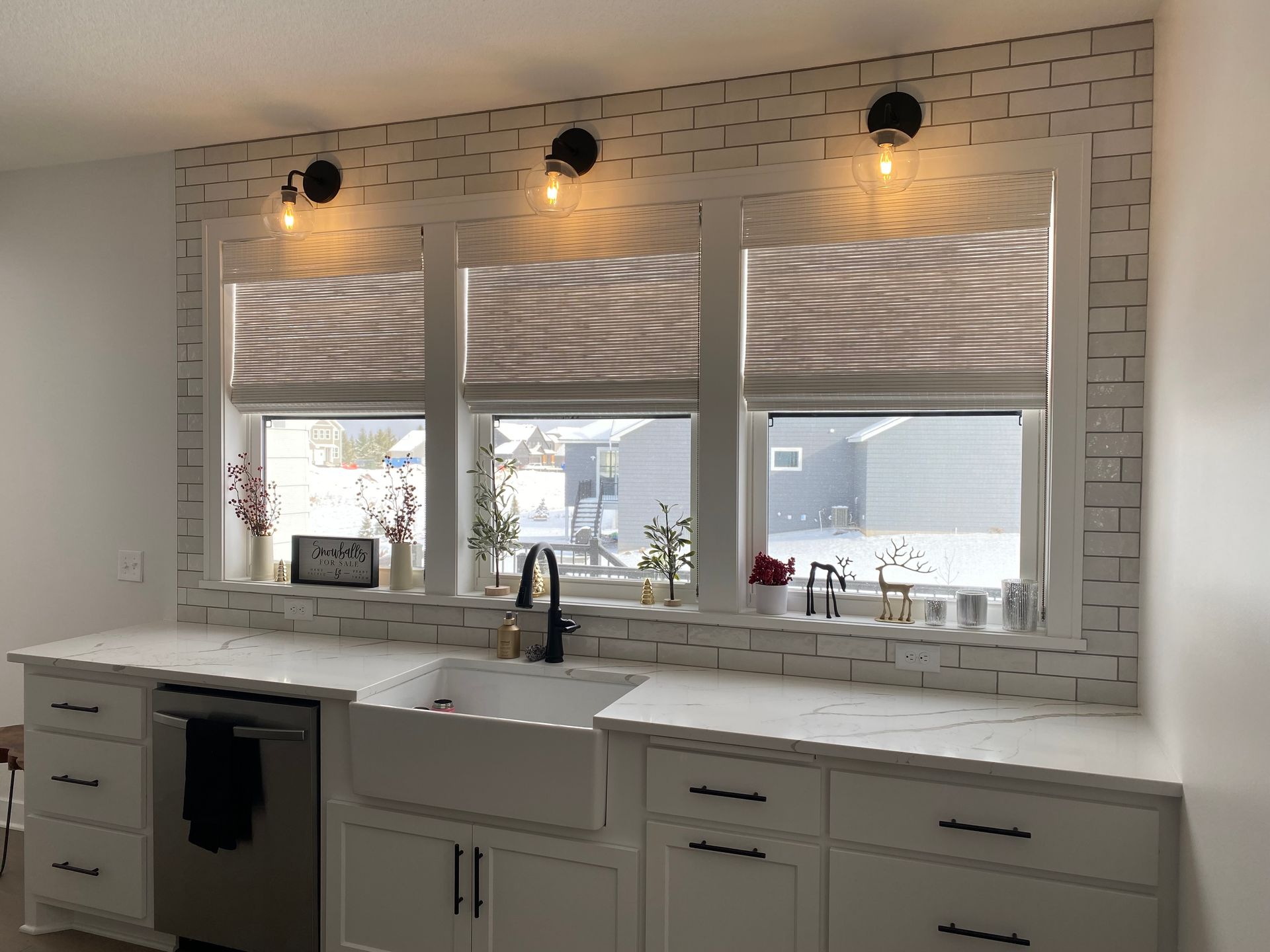 A kitchen with white cabinets , a sink , a dishwasher , and three windows.