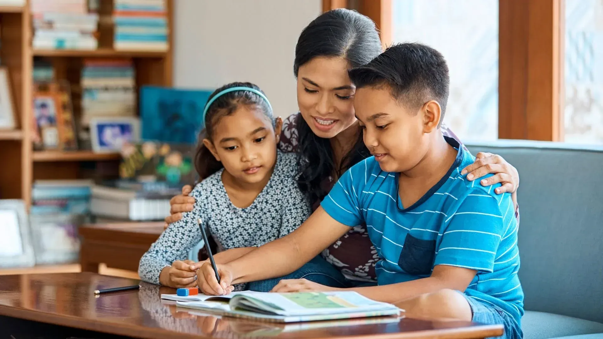 Woman helps two children with homework at a table.