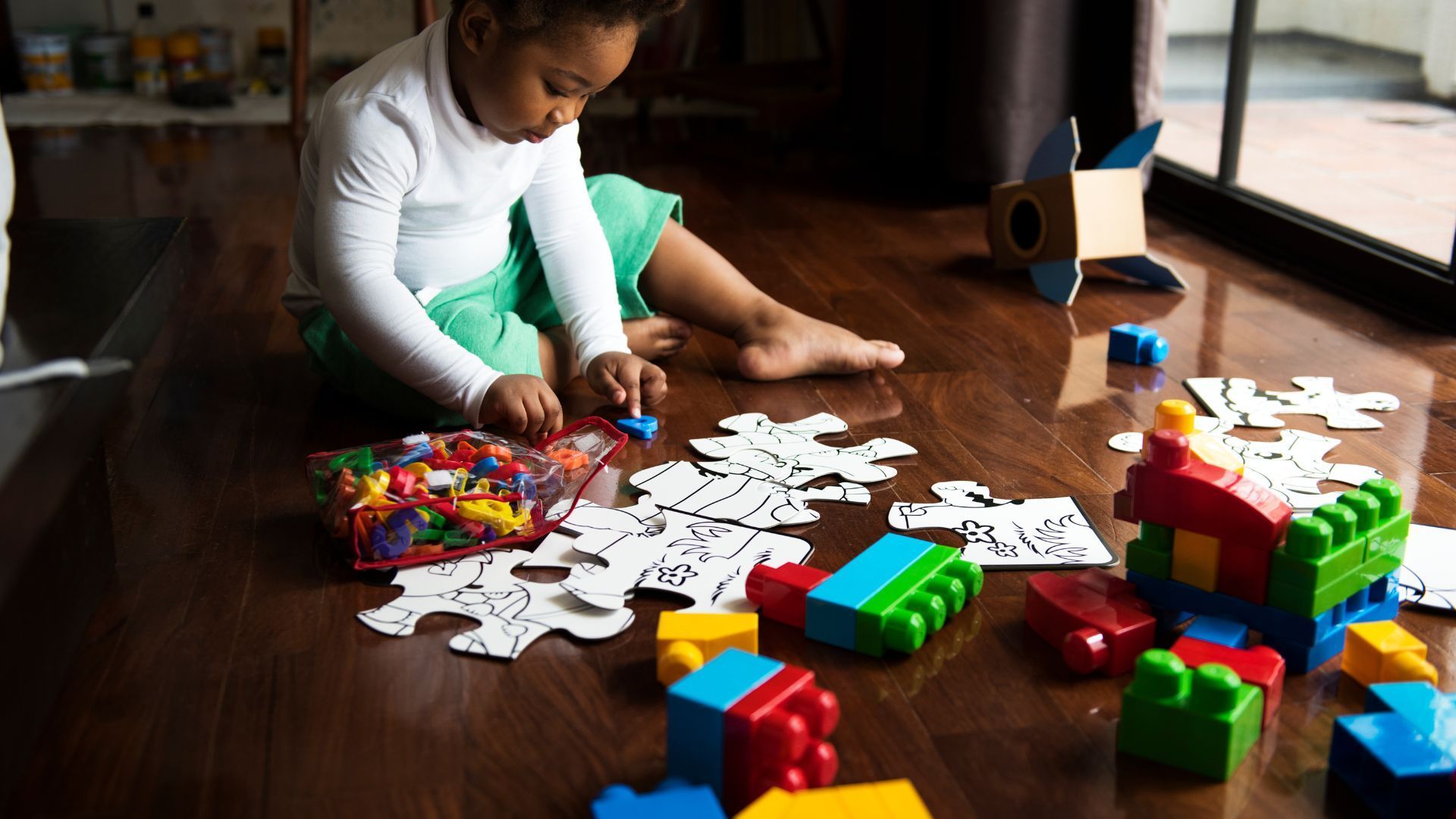 Child playing with puzzles and building blocks on a wooden floor.