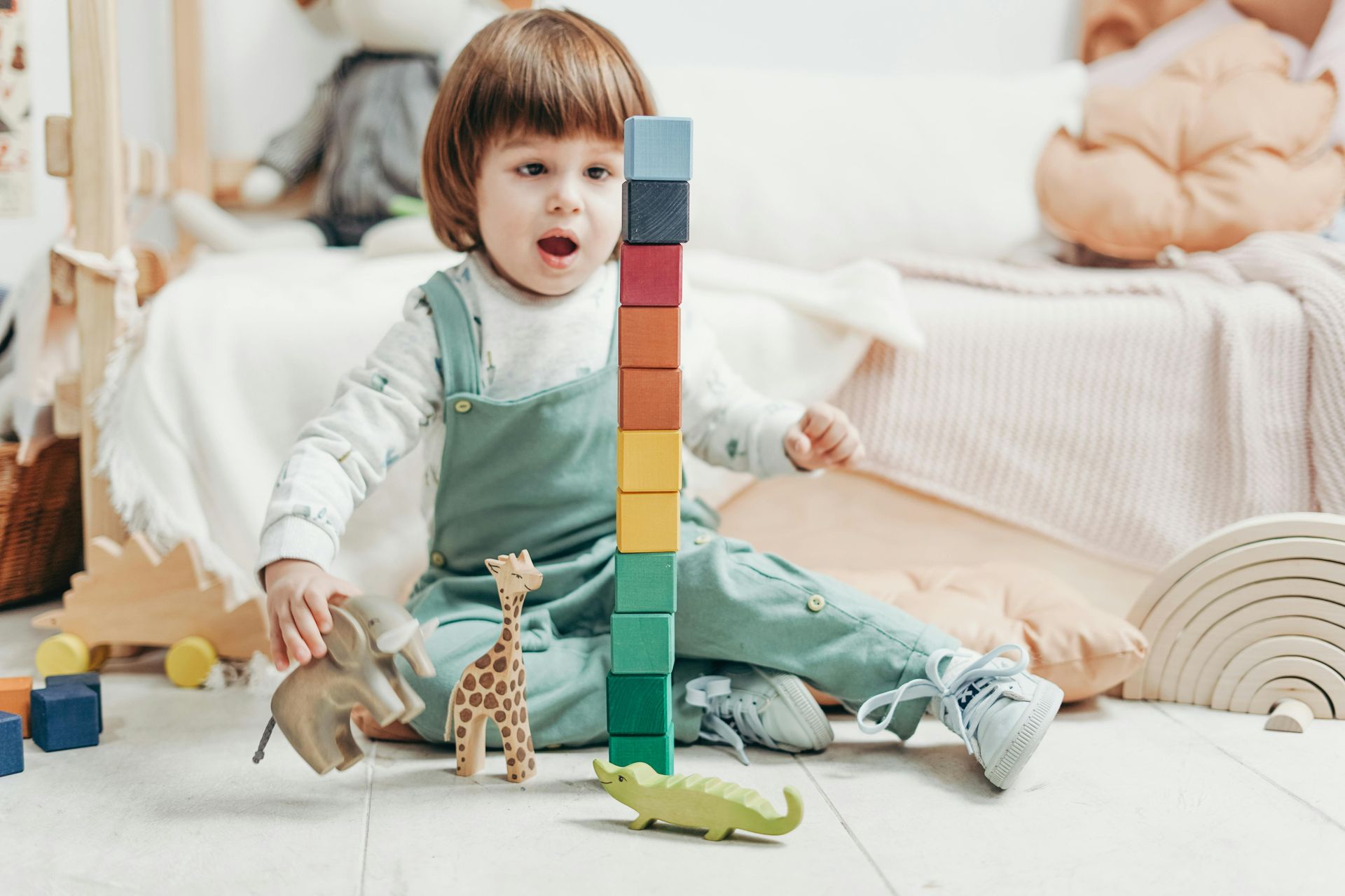 Child playing with colorful blocks, animals, and wooden toys in a bright room, blocks stacked high.