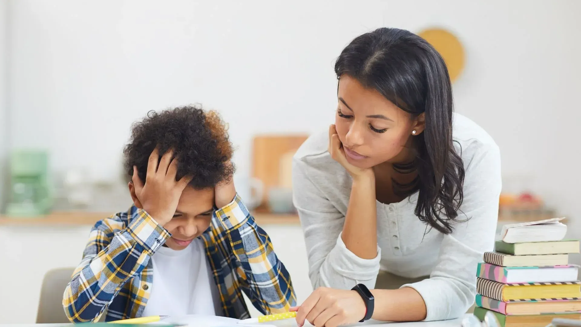 A person helping a student with homework; student looks frustrated with head in hands.