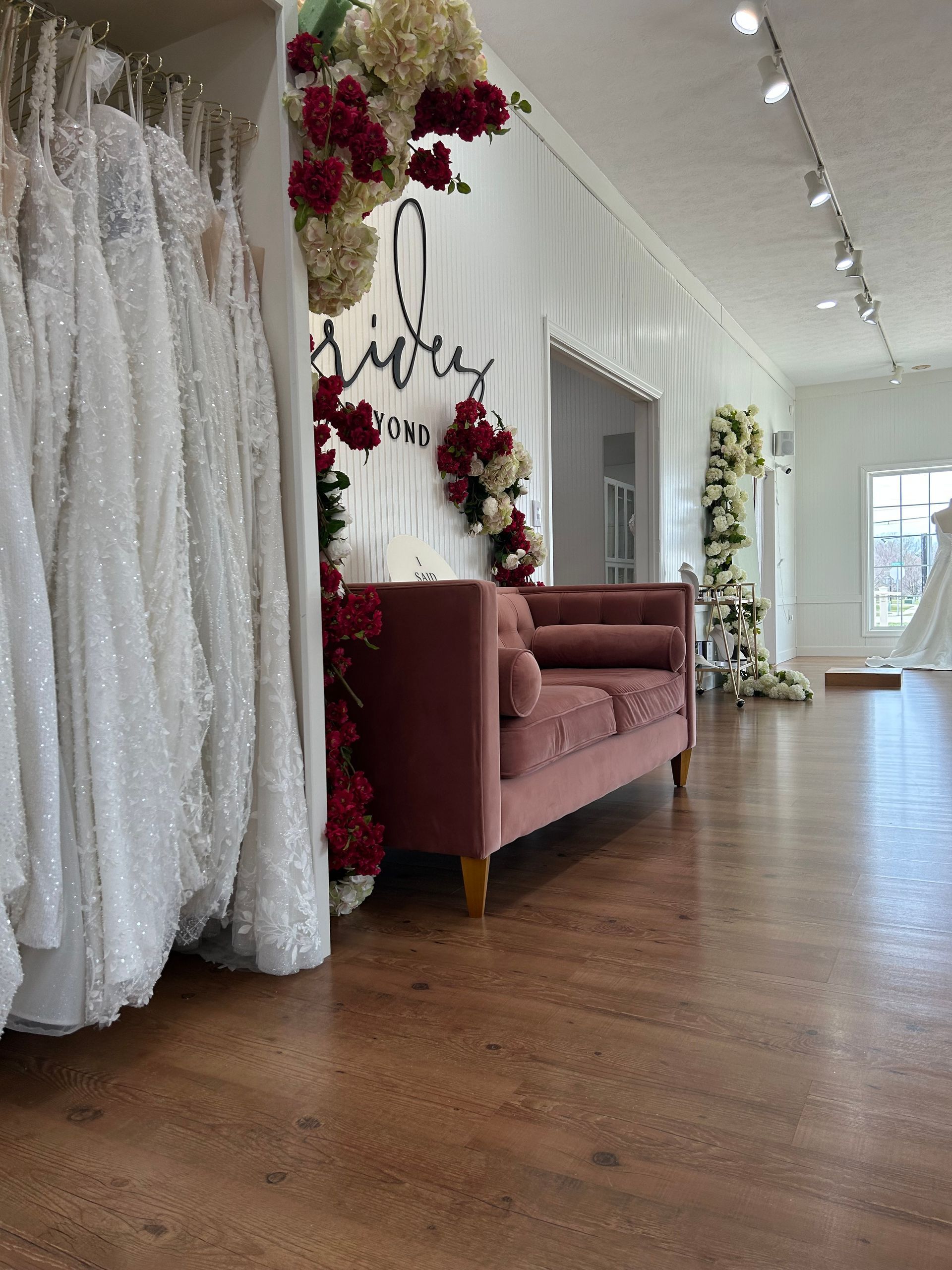 Interior of a bridal boutique with wedding dresses, a pink sofa, and floral decorations.
