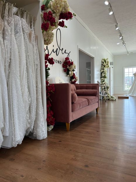 Interior of a bridal boutique with wedding dresses, a pink sofa, and floral decorations.