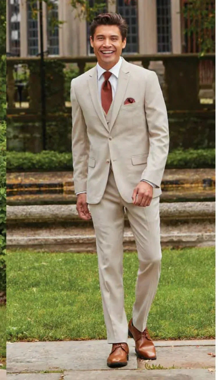 Man in tan suit smiling, walking outside, brick background.