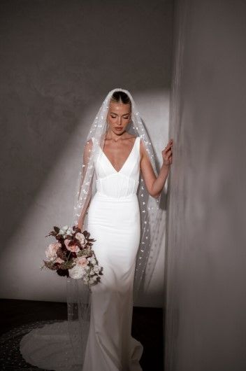 Bride in a white strapless gown with a thigh-high slit, smiling in a sunlit room.