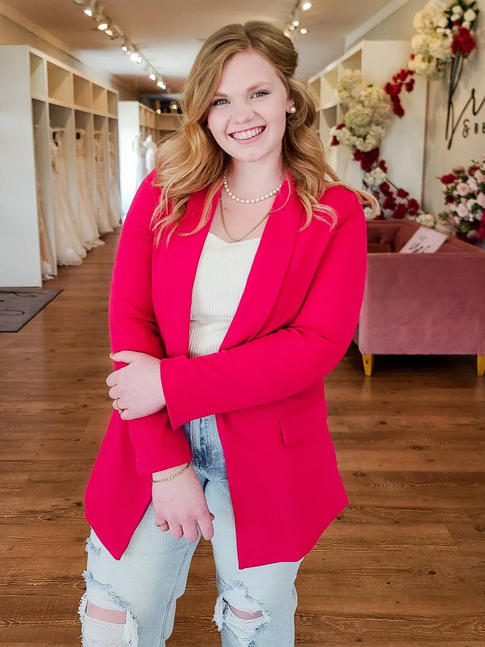Woman in pink blazer, jeans smiles in bridal shop.