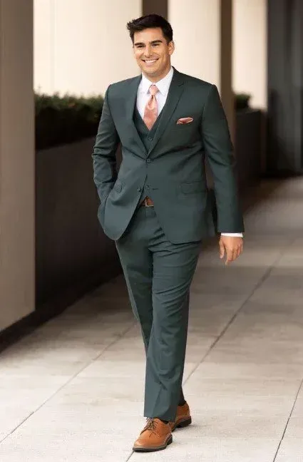 Man in green suit walking, smiling, on walkway; light brown shoes, peach tie and pocket square.