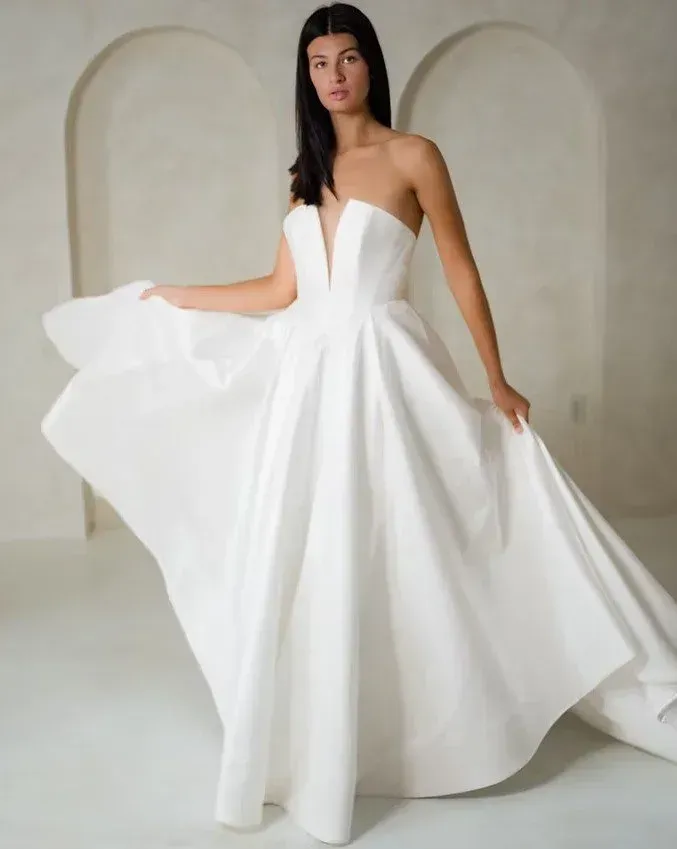 Woman in a white strapless wedding dress poses in a neutral-toned room.