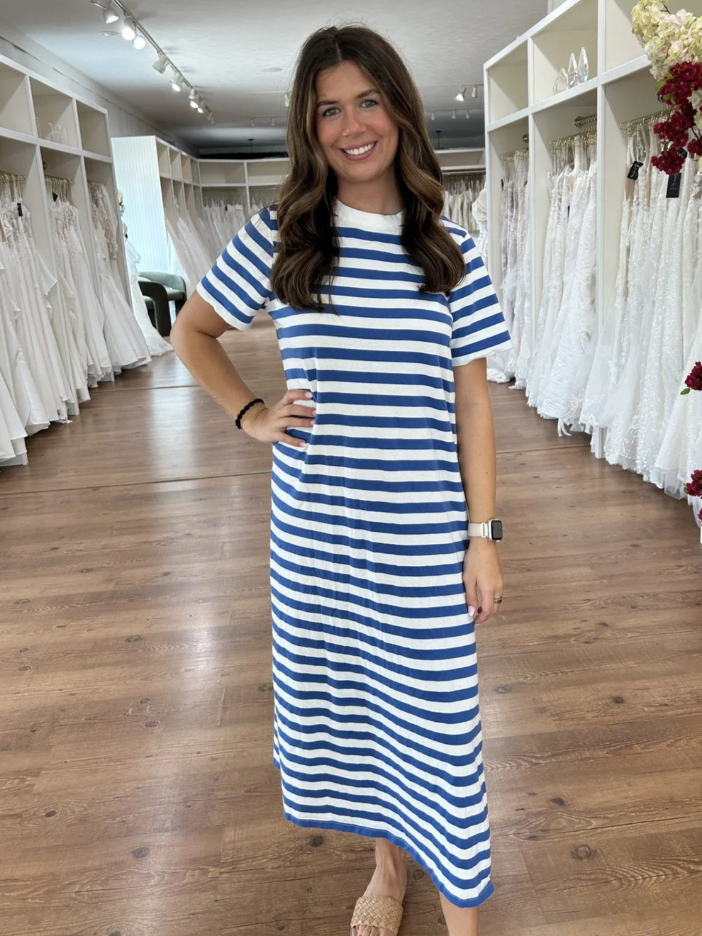 Woman in striped dress, smiling in a bridal shop, hands in pockets.
