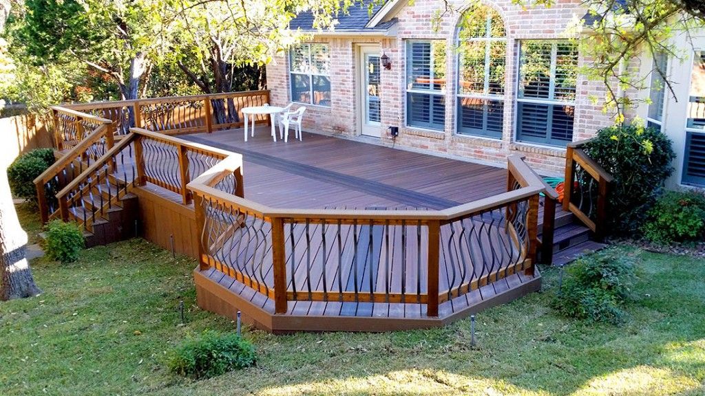 Wooden backyard deck with railings beside a house, surrounded by grass and trees