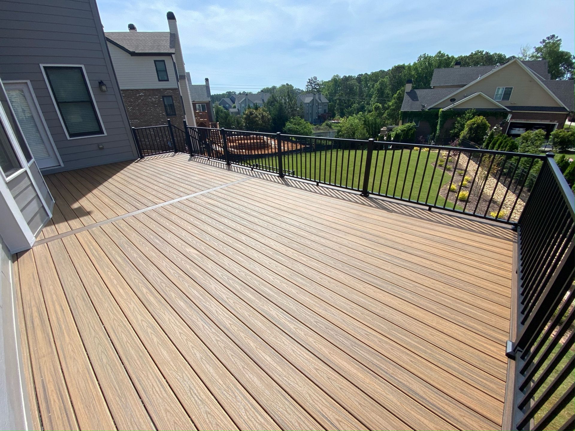 Spacious wooden deck with black railing beside a house, overlooking a grassy backyard and neighboring homes