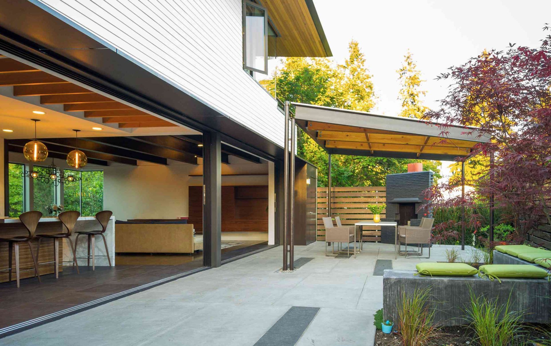 Modern patio with covered seating, concrete walkway, and landscaped garden in warm sunlight