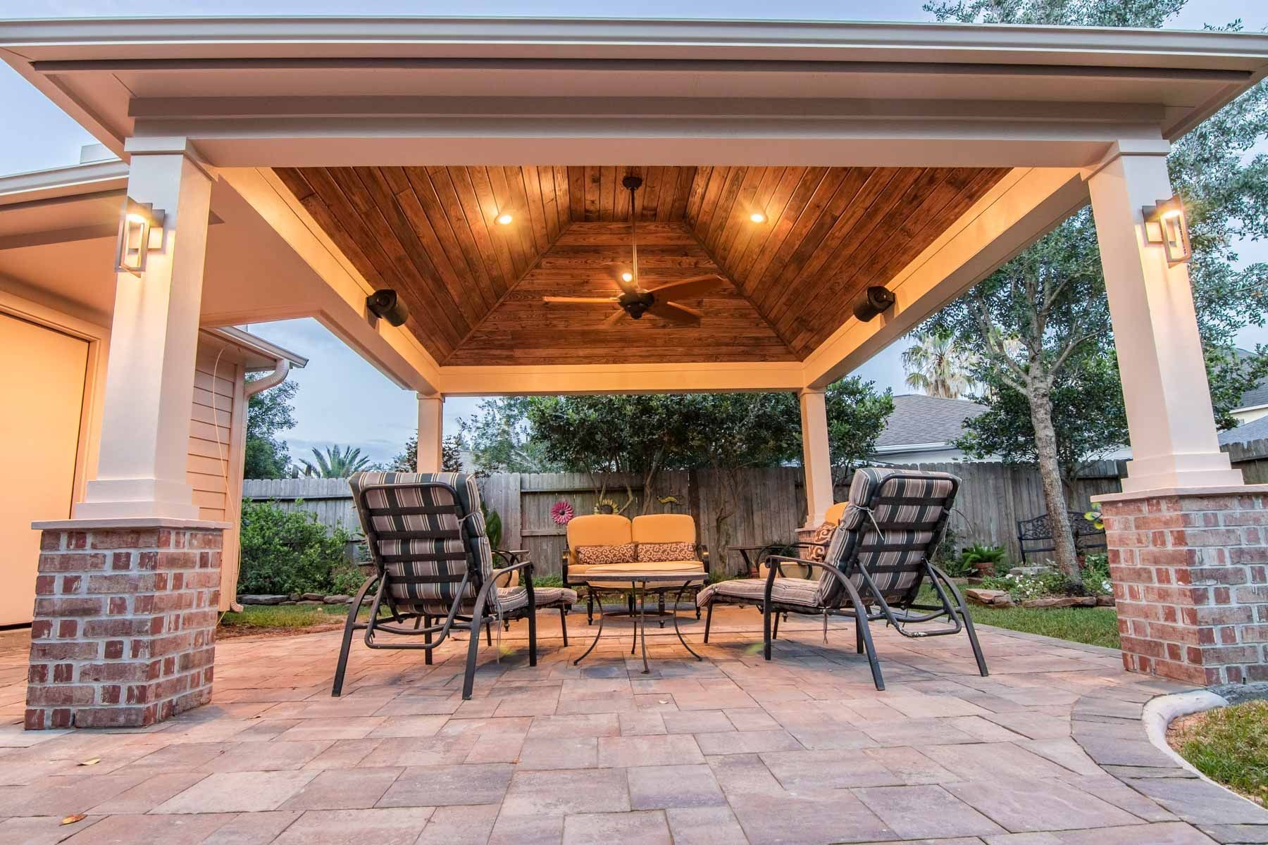 Covered patio with wicker seating, warm lights, and stone flooring at dusk