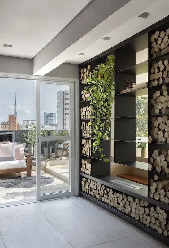 Interior with firewood storage, greenery, and an outdoor patio. Black shelving, light and dark wood.