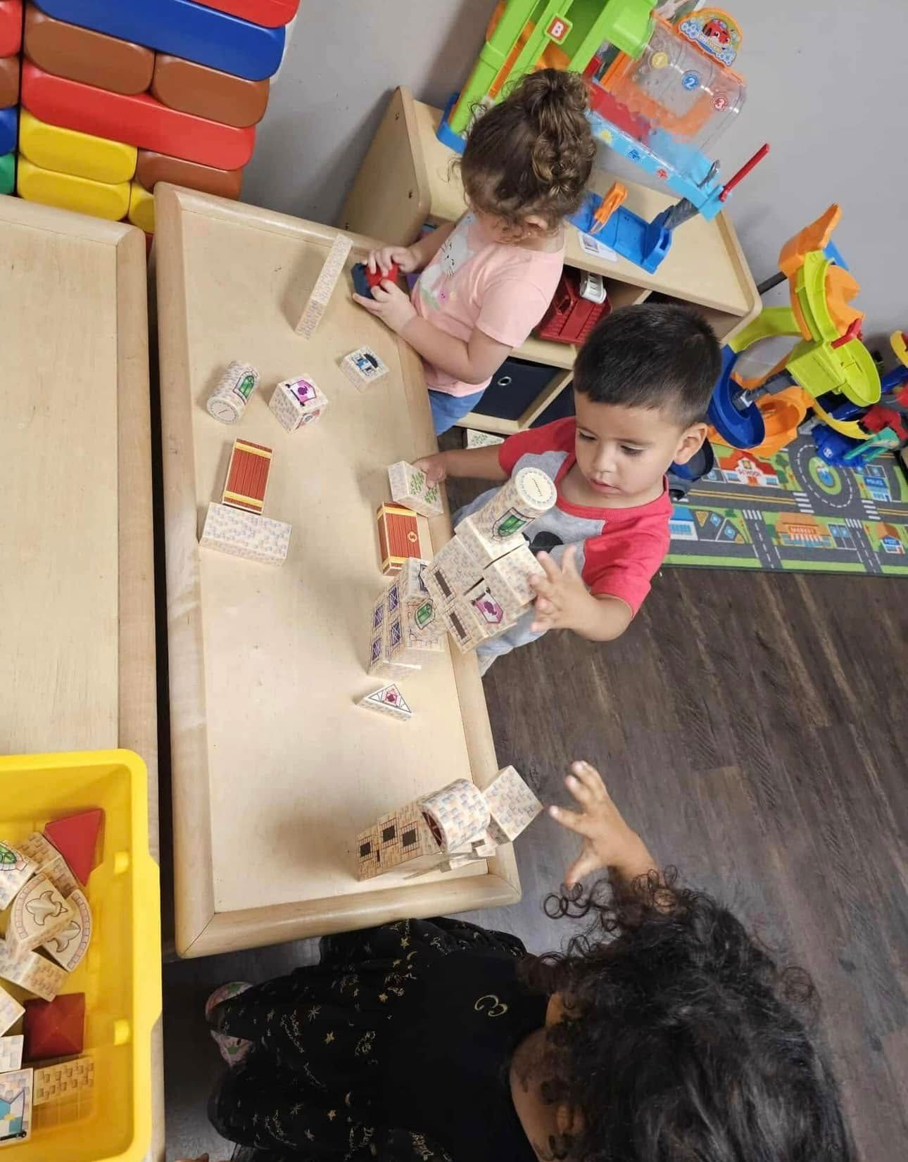 Children playing with blocks and toys at a table in a classroom.