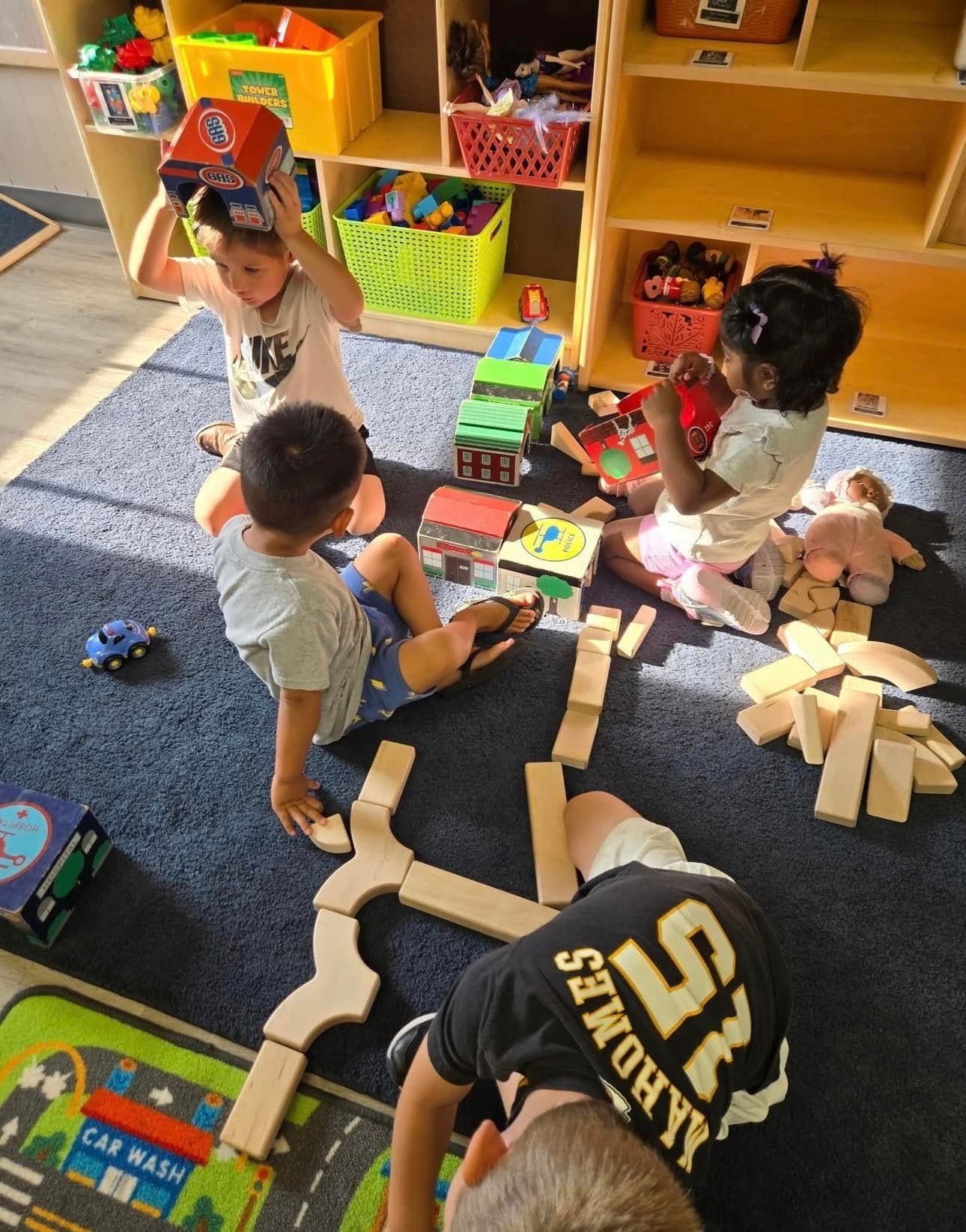Children playing with blocks and toys on a blue carpet in a brightly lit room with shelves.